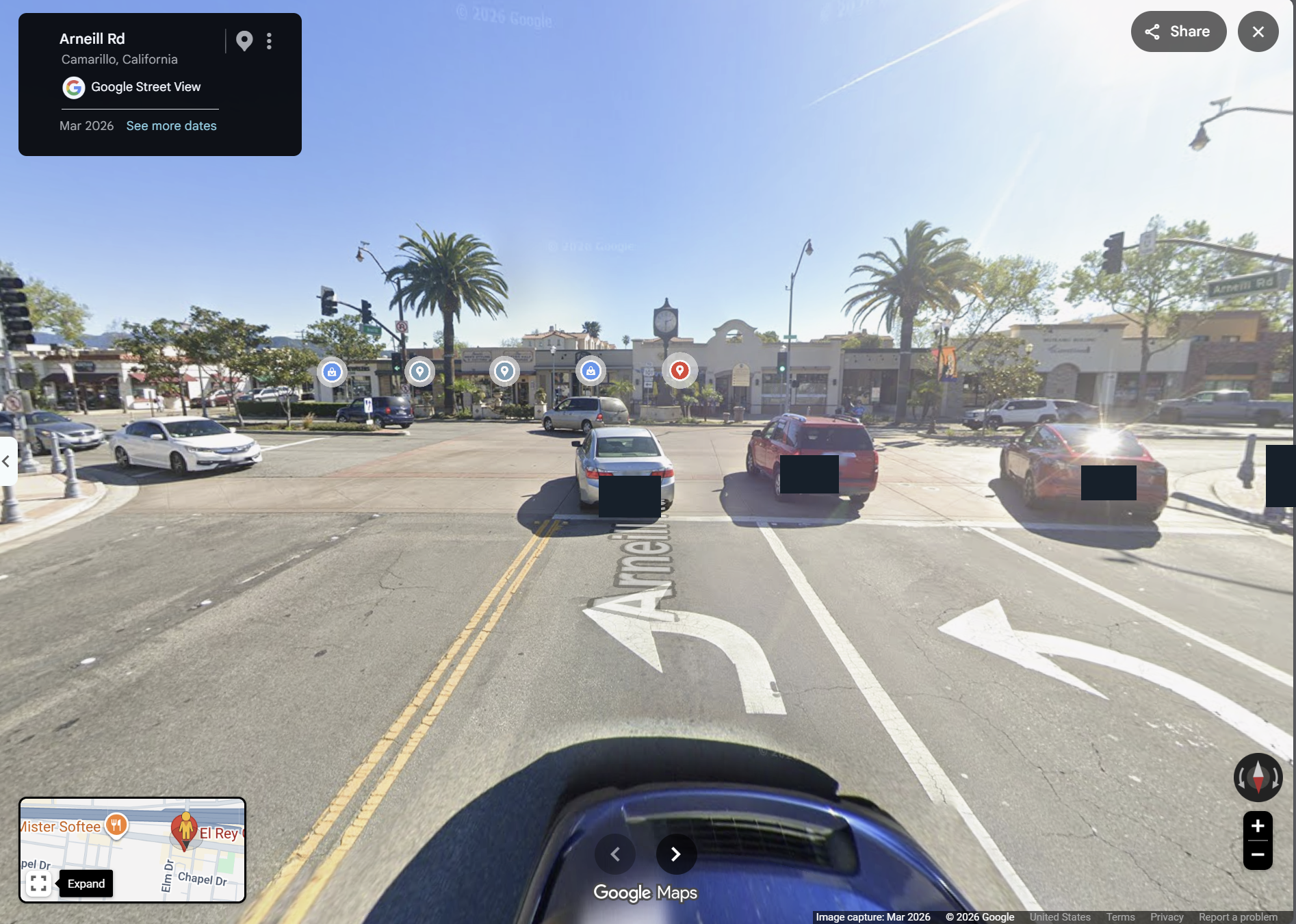March 2026 Street View from Arneill Rd toward Ventura Blvd: left and right turn arrows, traffic signals and the El Rey restaurant block across the T-junction. Incidental identifiers are masked.